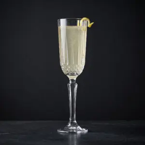 Diony flute Pasabahce con un French 75 e la scorza di limone sul bordo, su fondo scuro