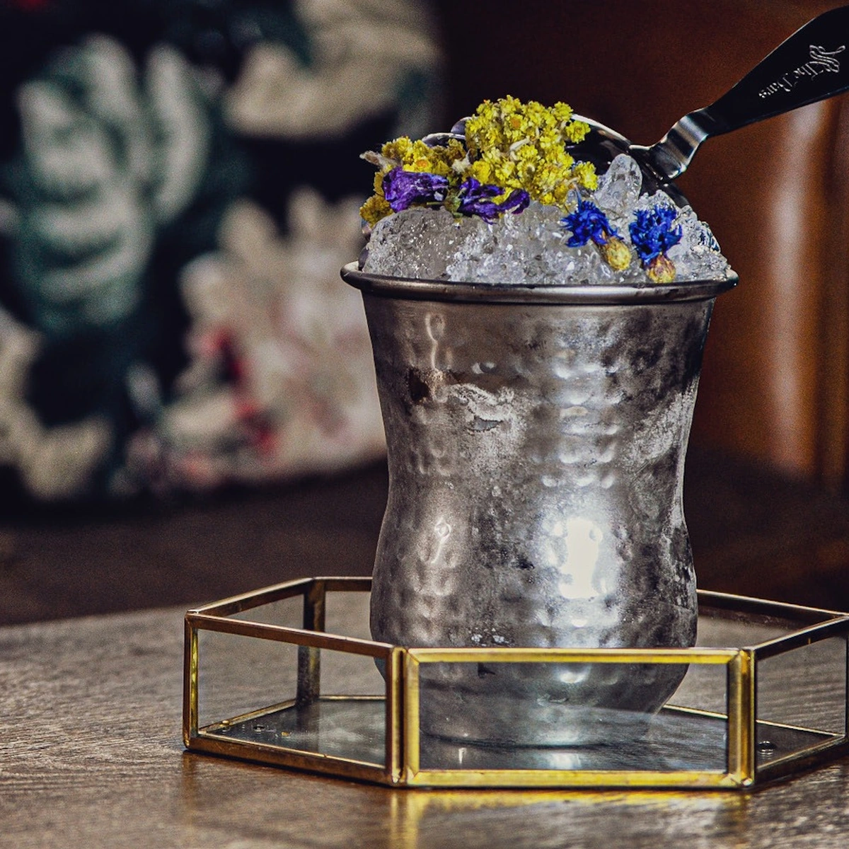 Julep cup martellata The Bars con ghiaccio tritato e fiori, su un vassoio in vetro e ottone