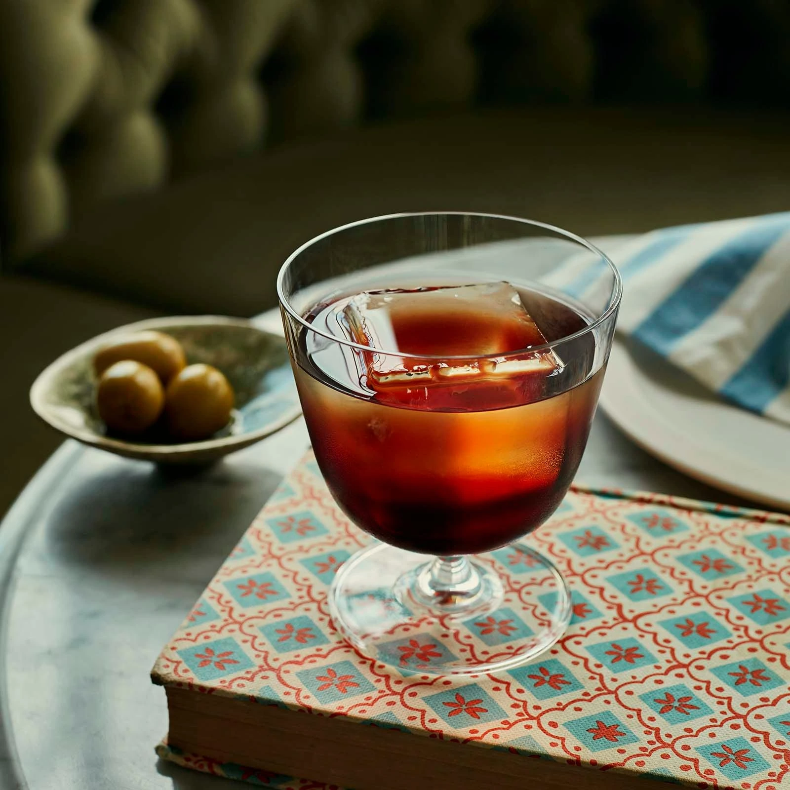Bicchiere old fashioned: calice old fashioned Bargiani NUDE 32 cl in cristallino, con un drink scuro e ghiaccio sul tavolo